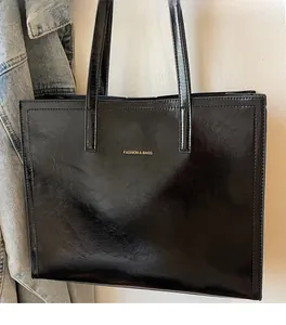 Detail der schwarzen Shopper-Tasche aus Kunstleder mit Golddruck an einer Jeansjacke