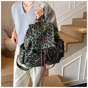 Detail of leopard print canvas backpack showing red cursive branding and drawstring closure
