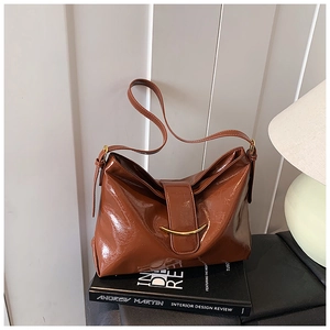 Gros plan du sac en cuir verni marron avec boucle dorée en croissant et détails plissés