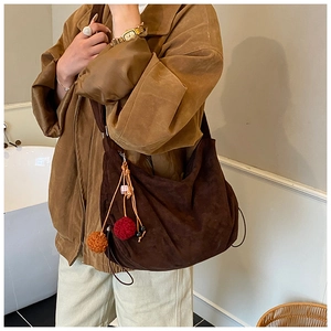 Detail of dark brown suede hobo bag with colorful pompom charms and drawstring sides