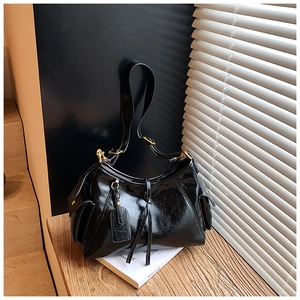 Detail of glossy black tote bag featuring retro strap accents and gold-tone metal hardware