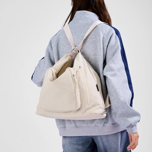 Close-up of beige versatile backpack showing multi-pocket zipper design and adjustable straps