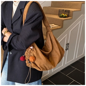 Detail of brown suede hobo bag with colorful pom-pom charms and drawstring side details