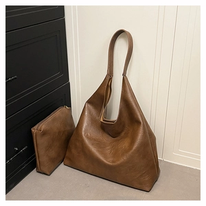 Detail of a large brown leather tote bag with matching zippered pouch on minimalist background