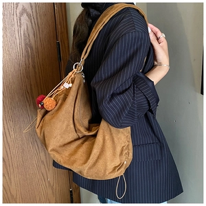 Close-up of brown suede hobo bag featuring decorative pompoms and metal ring adjustment