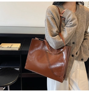 Detail einer großen braunen Tote-Bag aus glänzendem Leder mit goldener Metallplakette