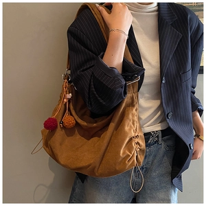 Close-up of brown suede tote bag featuring decorative colorful pom-poms and drawstring