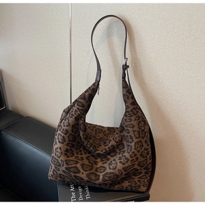 Detail of leopard print tote bag with brown leather strap against a textured wall