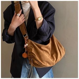 Brown faux suede crescent bag detail featuring side pleats and a plush ball charm