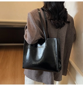 Detailansicht der schwarzen Lackleder-Einkaufstasche mit goldener Logo-Plakette am Model