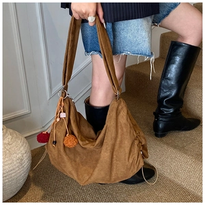 Detail of a brown suede tote bag with a colorful pom-pom charm and vintage slouchy design