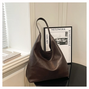 Detail of a large dark brown leather hobo tote bag on a black table with a modern backdrop