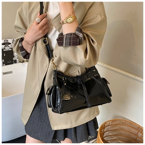 Detail of glossy black patent leather tote bag with side flap pockets and gold hardware