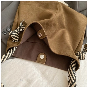 Detail of brown suede tote bag with woven shoulder strap and metal magnetic closures