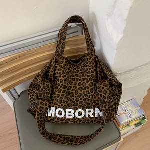 Détail du sac cabas en toile à imprimé léopard avec lettrage Moborn posé sur une chaise