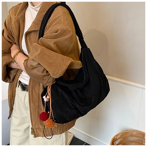 Detail of soft black tote bag with colorful plush ball charms and wide shoulder strap