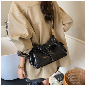 Detail of a black patent leather tote bag with gold hardware and side pocket on a model