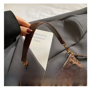 Detail of leopard print handbag showing brown leather handle and gold hardware buckles