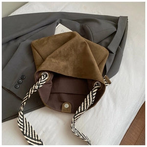 Detail of brown matte suede bucket bag with woven shoulder strap on a grey blazer