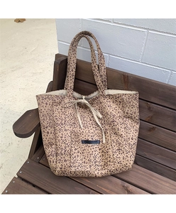 Close-up of leopard print suede tote bag with front pocket and drawstring on wooden bench