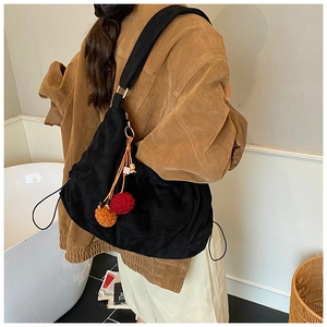 Detail of black suede tote bag featuring a colorful pompom and bear charm with wide strap
