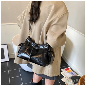 Detail view of a black patent leather tote bag styled on a shoulder in a modern setting