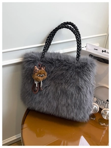 Detail view of grey plush tote bag with black handles and cute bear charm on a table