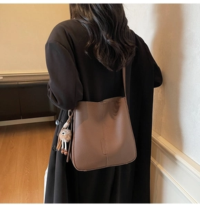 Détail du sac seau en cuir marron avec breloque peluche rigolote aux longues jambes