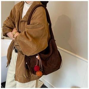 Close-up of a large dark brown suede hobo bag with drawstring and plush ball charm