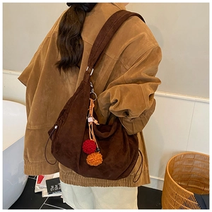Detail of a large brown suede hobo bag with colorful plush charms on the wide strap