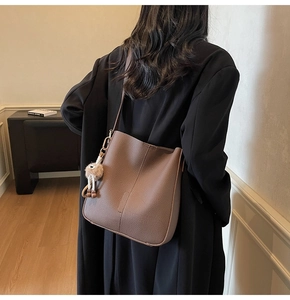 Gros plan d'un sac seau en cuir marron avec un charme en peluche sur un modèle
