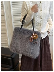 Close-up of grey faux fur tote bag with black woven handles and a plush doll pendant