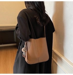 Sac seau marron en cuir grainé avec pompon en peluche porté sur l'épaule d'un modèle