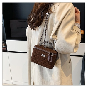 Brown suede vanity bag with quilted pattern and metal chain strap worn by a model