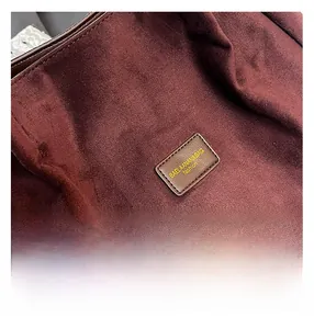 Close-up of dark burgundy suede tote bag with brown leather logo and fine stitching
