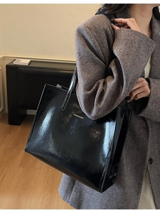 Große schwarze Tragetasche aus glänzendem Lackleder mit Logo für den täglichen Weg