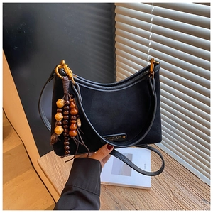 Détail du sac demi-lune noir mat avec finitions dorées et pompon à perles sur bois