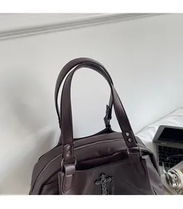 Detail view of smooth leather handle and metal cross pendant on large brown tote bag