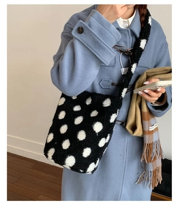 Détail du sac seau en peluche noir à pois blancs porté par un mannequin en manteau bleu