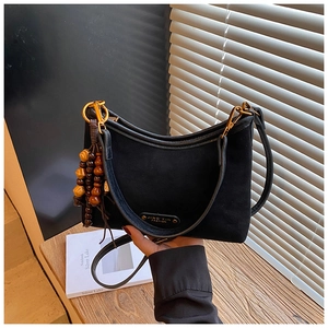 Detail of matte black suede crescent bag featuring wooden bead tassels and gold chain buckle