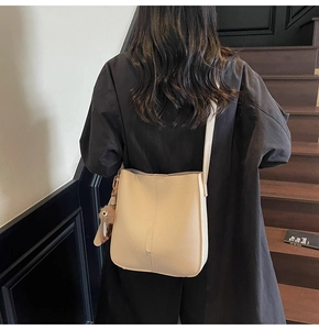 Détail du sac seau crème avec texture en cuir grainé et pompon marron décoratif