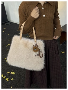 Detail of plush cream faux fur tote bag with woven handles and leopard charm on autumn leaves