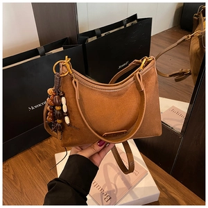 Détail d'un sac à main en daim marron avec accessoires dorés et pompon en perles bois