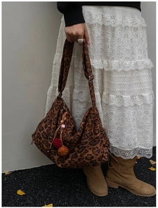 Detail view of leopard print tote bag with colorful pom-pom charms in autumn street setting