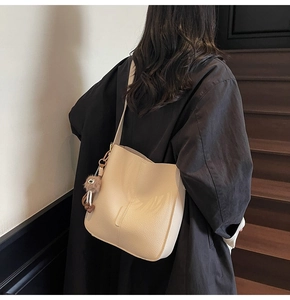 Sac seau beige tendance avec texture litchi présenté dans un décor d'escalier sobre