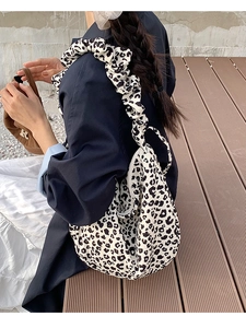 Detailed view of leopard print crescent bag with ruffled shoulder strap on a wooden bench