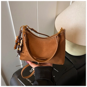 Détail d'un sac demi-lune en daim marron avec gland en perles de bois et texture gaufrée