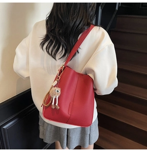 Détail du sac seau rouge avec texture litchi et charmant pendentif en peluche sur l'escalier