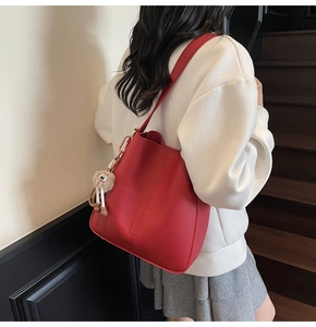 Sac seau en cuir rouge avec large bandoulière et pompon, porté par un mannequin