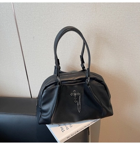 Detail of gothic black pebbled leather handbag featuring metal cross and chain accents